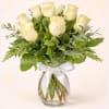 White roses arranged in a clear glass vase with a white ribbon