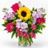 Bright mixed bouquet with sunflowers, pink roses, and lavender flowers in a glass vase