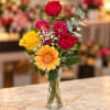 Mixed bouquet of roses, gerbera daisy, and mums in a clear glass vase