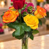 Bouquet of yellow and orange roses with a red rose in a clear glass vase