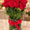 Red roses arranged in a clear glass vase with a red ribbon