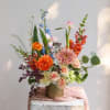 Mixed bouquet in a gold vase with orange, pink, blue, and white blooms