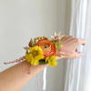 Wrist corsage with orange and yellow flowers on a white ribbon
