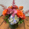 Orange roses and pink orchids in a green vase with blue hydrangea
