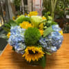 Blue hydrangeas and yellow roses in a glass vase with sunflowers