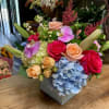 Mixed bouquet with roses, orchids, hydrangea, and lilies in a square vase