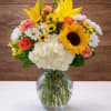Mixed bouquet of yellow lilies, sunflowers, roses, daisies, and hydrangea in a glass vase