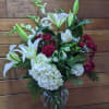 White lilies, white hydrangea, and burgundy roses in a glass vase