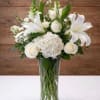 White floral arrangement in a clear glass vase with roses and lilies