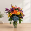 Colorful mixed bouquet in a clear glass vase with lilies, roses, and hydrangea