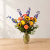 Colorful bouquet of roses, sunflowers, and blue delphinium in a glass vase