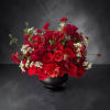 Red rose arrangement in a black vase with small white filler flowers