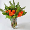 Orange roses in a clear glass vase with green foliage