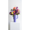 Colorful bouquet in a purple handled tumbler on a white pedestal