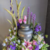 Floral urn arrangement with pink lilies and roses around a gray cremation urn