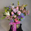 Mixed bouquet of pink, purple, and blue flowers in a glass vase with a pink ribbon