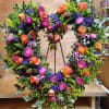 Large floral wreath with orange roses, pink blooms, and purple accents