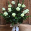 White roses arranged in a glass vase with a white ribbon