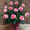 Pink roses arranged in a glass vase with a pink ribbon