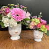 Two floral arrangements in white face vases on a wooden table