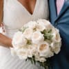 Bride holding a white rose bouquet beside a man in a blue suit
