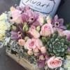 Pink roses and purple orchids arranged with succulents in a wooden box