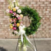 Floral wreath on a stand with pink, yellow, and white blooms