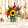 Colorful bouquet with a sunflower, roses, and purple blooms in a glass vase