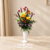 Mixed bouquet in a white pedestal vase with red, yellow, purple, and green blooms