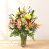 Mixed bouquet of yellow roses, orange lilies, and pink blooms in a glass vase