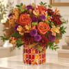 Orange roses and mixed fall flowers in a patterned glass vase