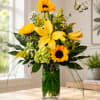 Yellow lilies and sunflowers arranged in a clear glass vase