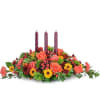 Low floral centerpiece with three burgundy candles and orange blooms