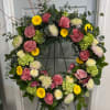 Large floral wreath with pink roses, yellow daisies, and green hydrangeas on an easel