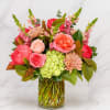 Mixed pink and coral flowers arranged in a clear glass vase