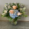 Mixed bouquet of peach roses, blue hydrangea, and small white daisies in a glass vase