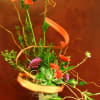 Tall floral arrangement with orange blooms in a square vase