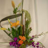 Tall floral arrangement with orange lilies, roses, and purple orchids