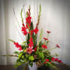 Tall floral arrangement with red gladiolus, pink lily, and green chrysanthemums in a white vase