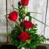 Red roses arranged in a white vase with green foliage