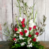 Tall floral arrangement with red roses and white flowers in a low black container