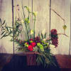 Mixed floral arrangement with red roses, white blooms, and pinecones in a rustic container