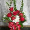Red roses and white flowers in a glass vase with a red ribbon