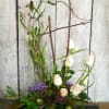 Tall floral arrangement with white roses and purple accents in a pink vase