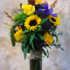Tall bouquet of yellow roses, sunflowers, and purple flowers in a glass vase
