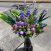Tall purple and blue floral arrangement in a black vase