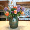 Tall floral arrangement with roses, purple allium, and berry branches in a green vase