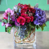 Bouquet of red roses, purple hydrangeas, and pink blooms in a clear square vase