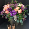 Mixed bouquet of peach roses and purple flowers in a dark vase