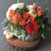 Orange and white floral arrangement in a pumpkin centerpiece with small pumpkins